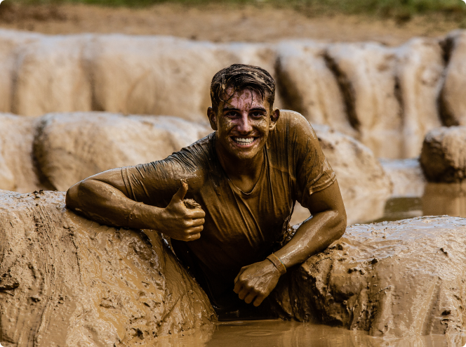 Junge, der unter dem Schlamm sitzt und seinen Daumen hochhält während des Strong Viking Mud Runs.