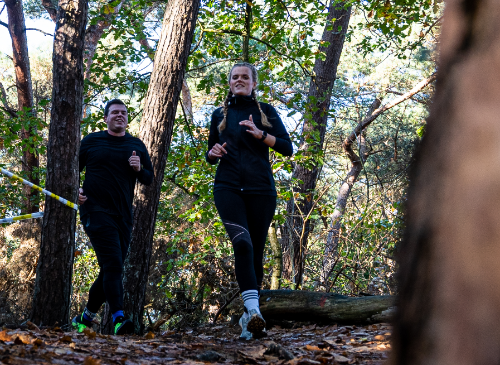 een man en vrouw die door het bos rennen tijdens de trail run van strong viking