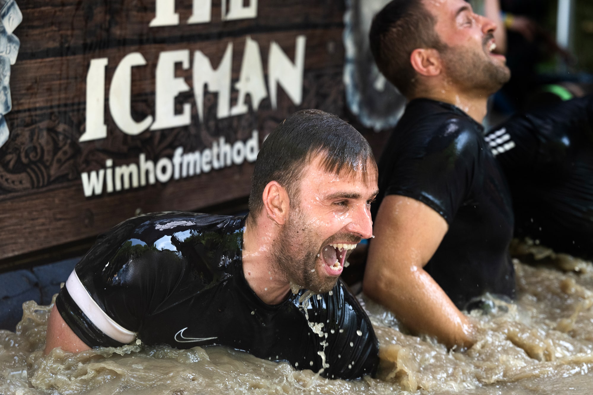 Twee mannen die door het ijsbad van het obstakel the iceman van de wim hof ademhalingsmethode heen duiken